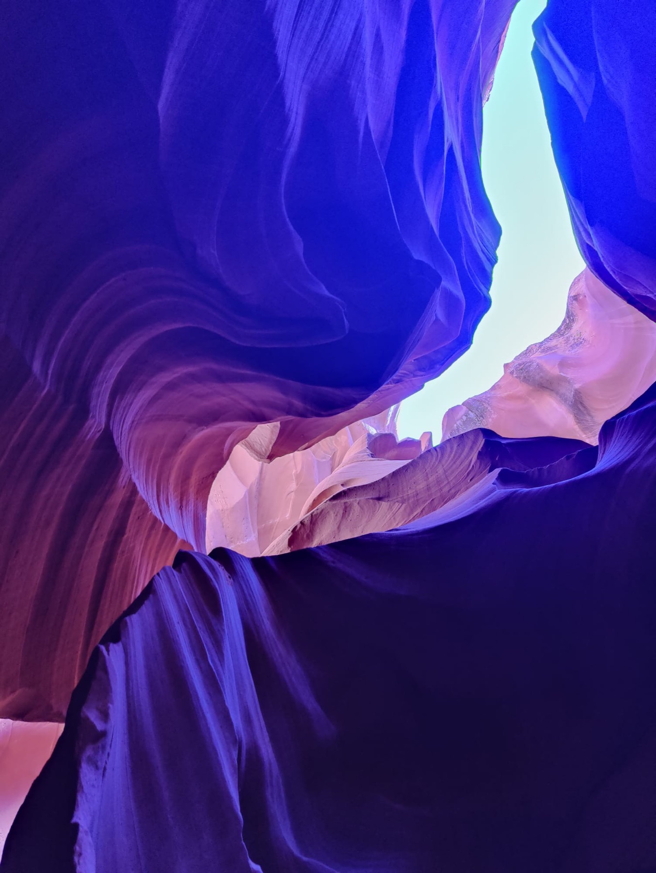 Violet sandstone walls curling up toward a sliver of sky in a slot canyon