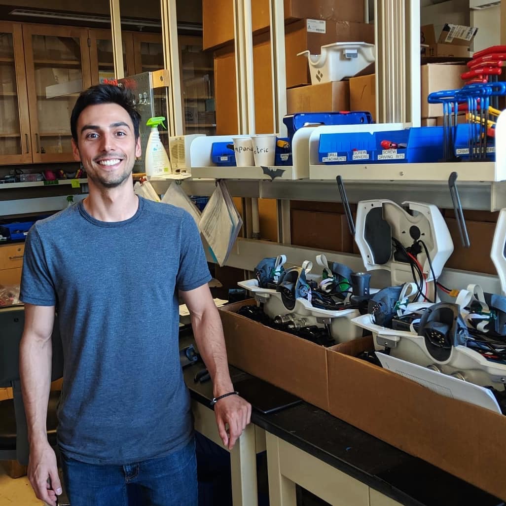 Volga smiling in a lab next to shelves of small field robots